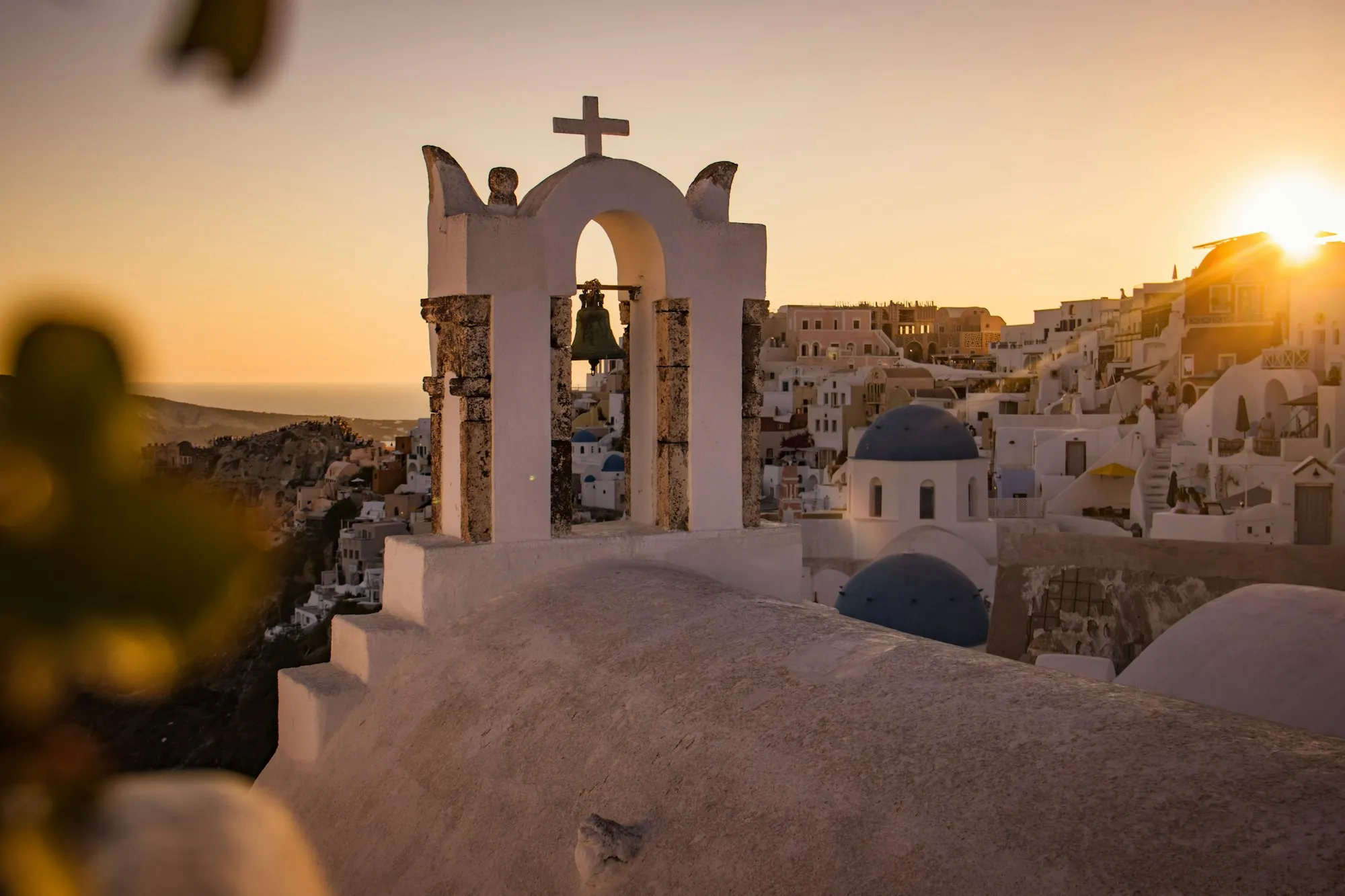 Campanário branco e cúpulas azuis de Oia, Santorini, ao pôr do sol