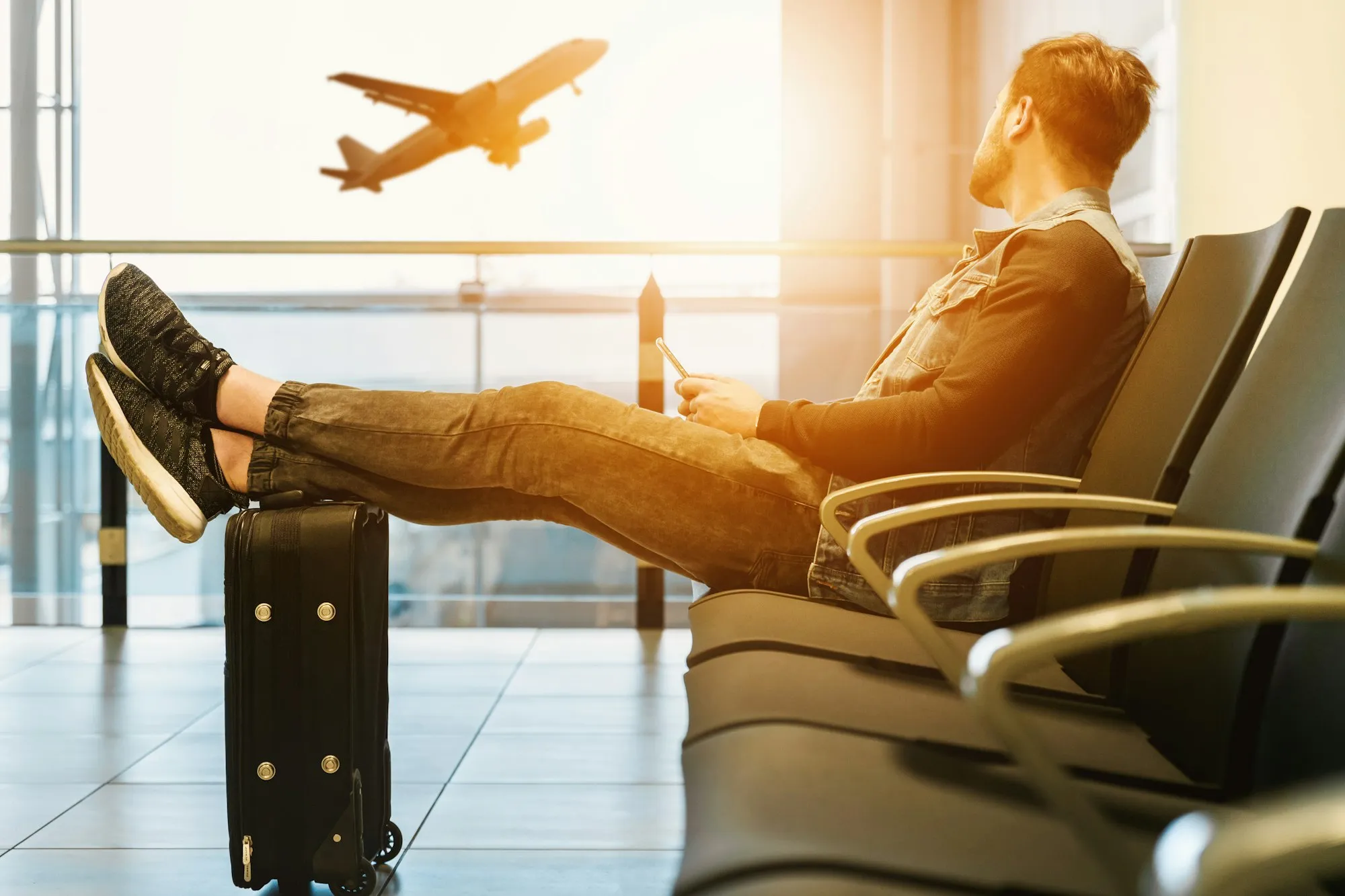 Viajante sentado no aeroporto com a mala, observando um avião na pista